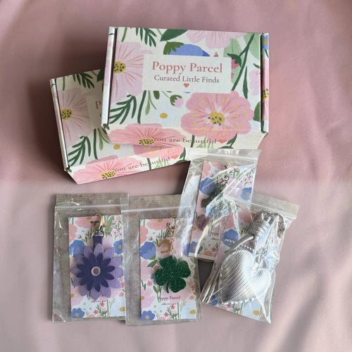 Poppy Parcel classic mystery box with floral mailer boxes and individually packaged bag charms on pink fabric.