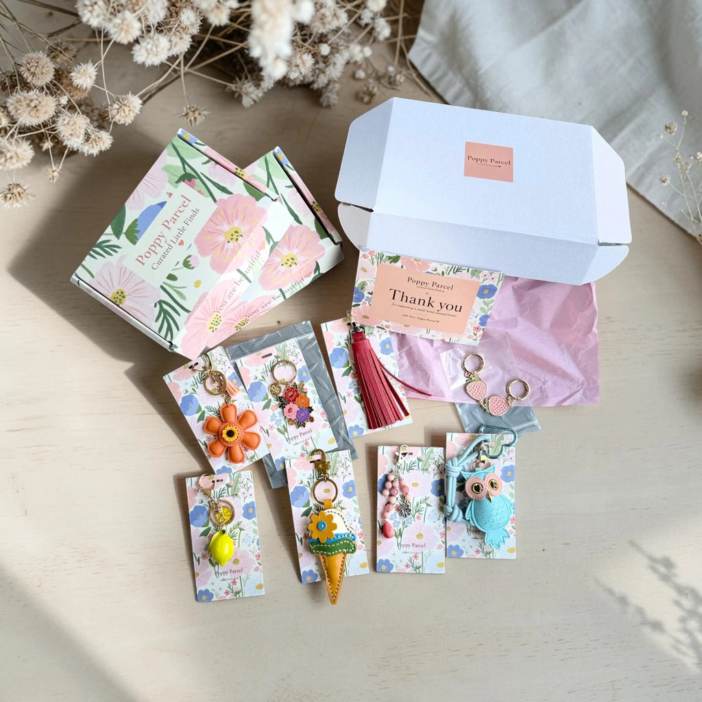 Poppy Parcel Deluxe bag charm mystery box unboxed, showing floral gift packaging, pink tissue paper, and a curated set of keychains and charms in pastel colors